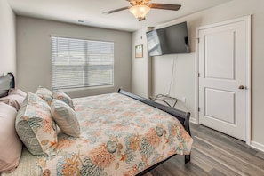 A bedroom with a bed, a ceiling fan, a TV on the wall, and a door. - 2 Mi to Sea & Sand! Modern New Build in Surfside (Surfside Beach)