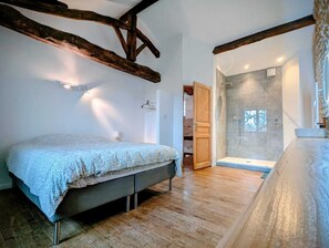 Un dormitorio con cama, vigas de madera, ducha y baño con bañera.
