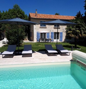 A pool with lounge chairs and umbrellas, a stone building with blue shutters, and a clear blue sky. - Charming holiday house with stunning view and heated swimming pool. (Palluaud)