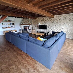 A modern living room with a large blue sectional sofa, a fireplace, a stone wall, and a wooden ceiling.