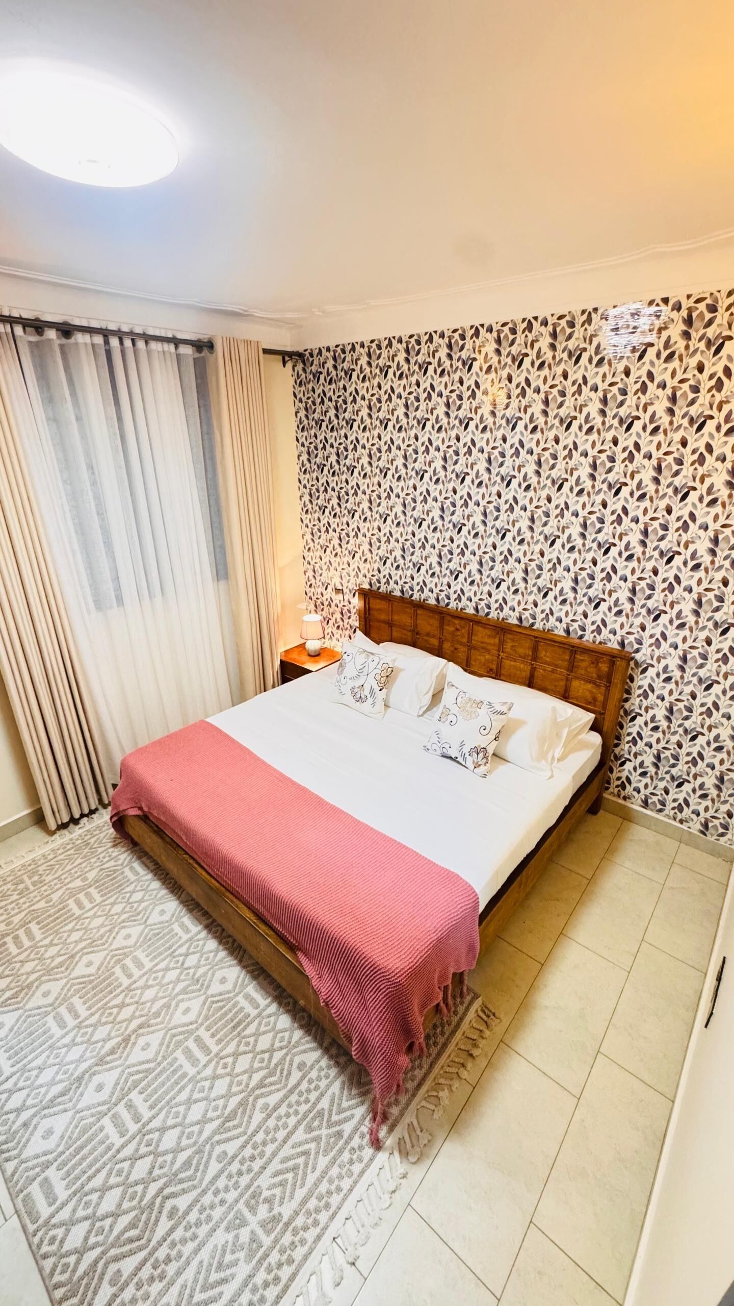 A hotel room with a bed, patterned wallpaper, curtains, and a patterned rug.