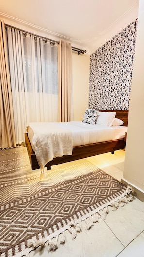Ein Schlafzimmer mit Bett, Vorhängen, einer Wand mit Muster und einem Teppich.