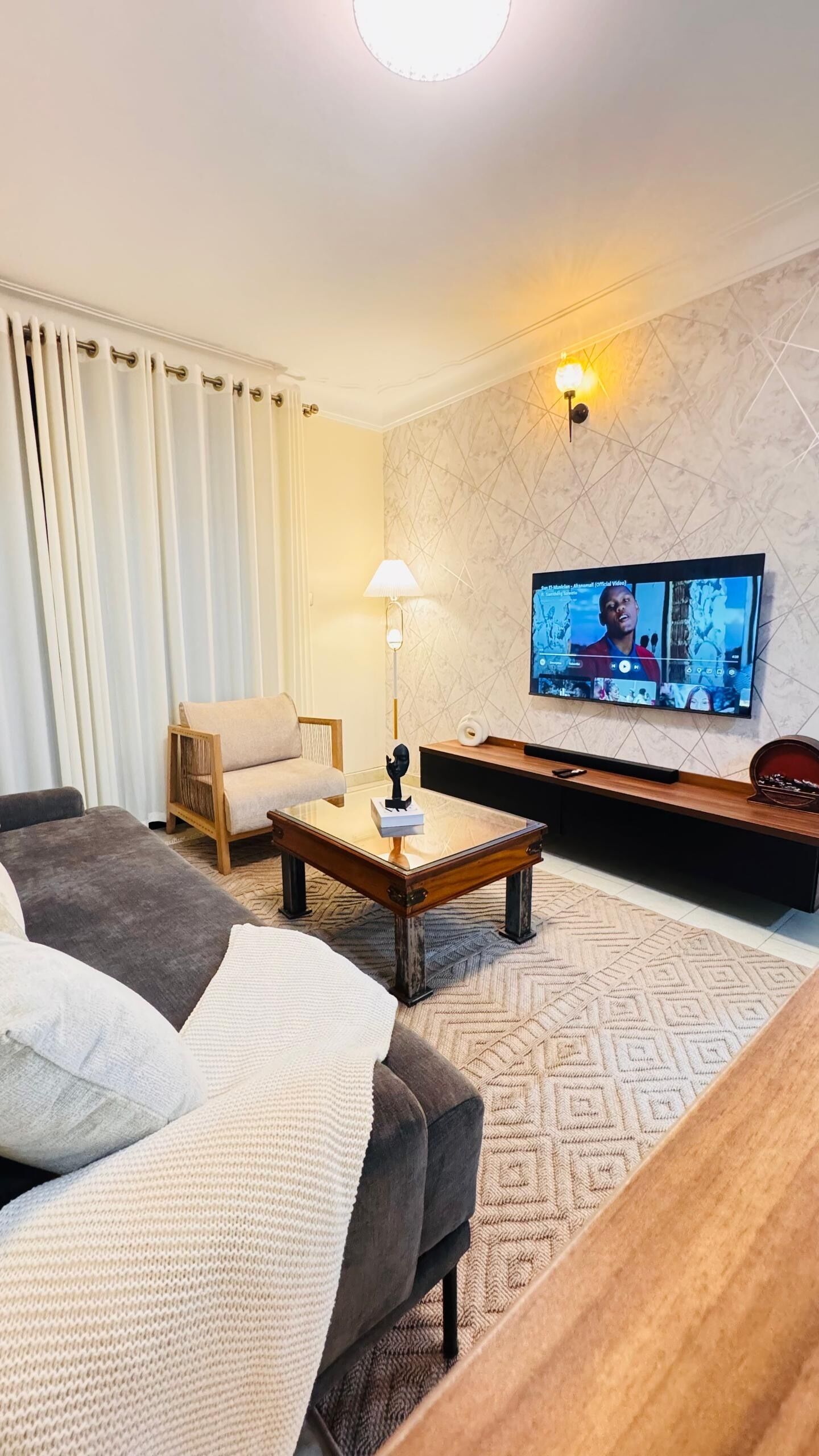 Un salon moderne avec un canapé, une table basse, un téléviseur et un mur décoré d’un motif.