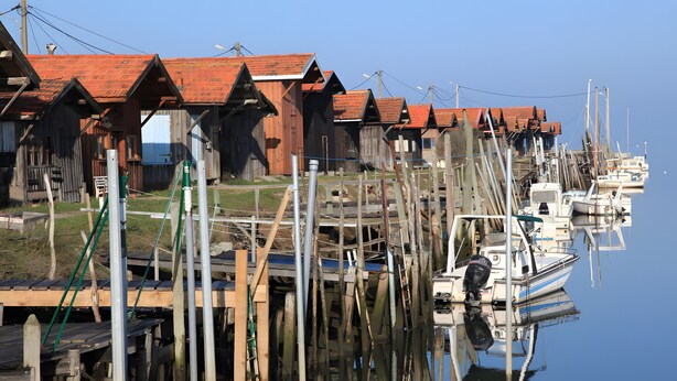A waterfront with wooden buildings and boats docked. - Guest Room "Les Pins" with Shared Terrace, Wi-Fi, and Air Conditioning (Gujan-Mestras)
