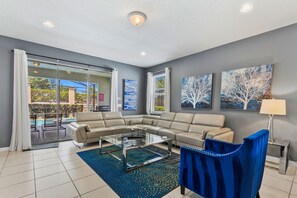 Ein modernes Wohnzimmer mit einer Eckcouch, einem Glastisch und Blick auf einen Pool und eine Außenanlage.
