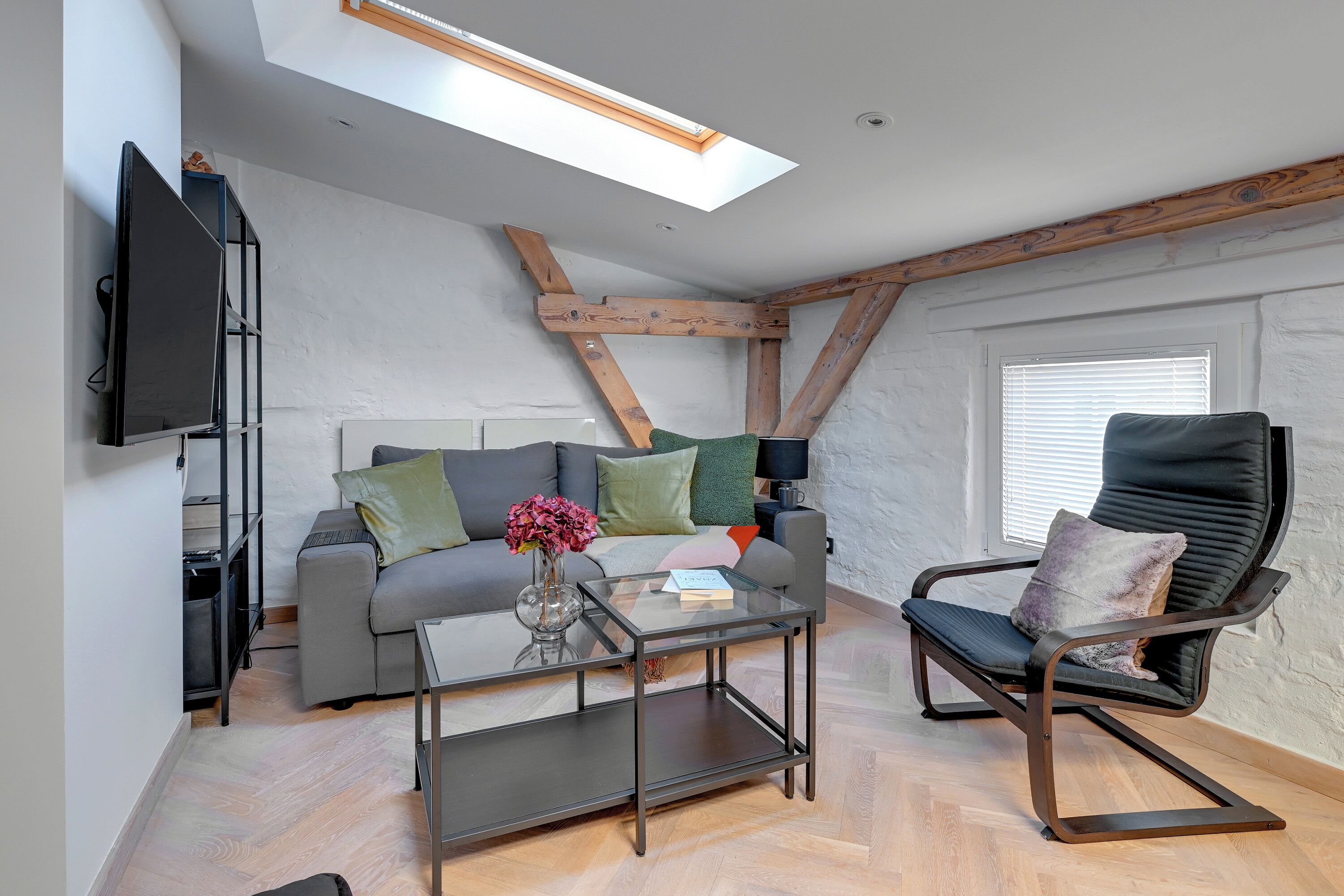 A loft-style room with a sloped ceiling, a sofa, a chair, a coffee table, and a television.