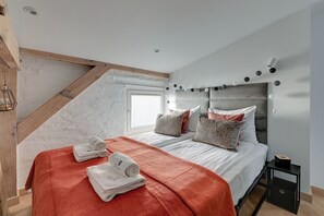 A bedroom with a sloped ceiling, a bed with white bedding, a red blanket, and a headboard with lights. - Modern Attic - Cozy Top Floor Sopot (Sopot)