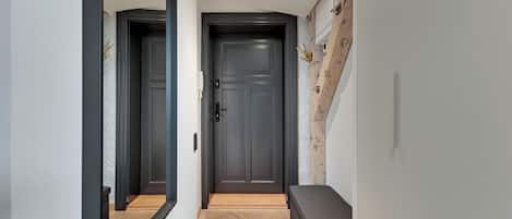 A hallway with a dark door, a bench, and a mirror reflecting the door.
