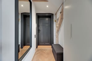 Um corredor com uma porta escura, um banco e um espelho refletindo a porta.
