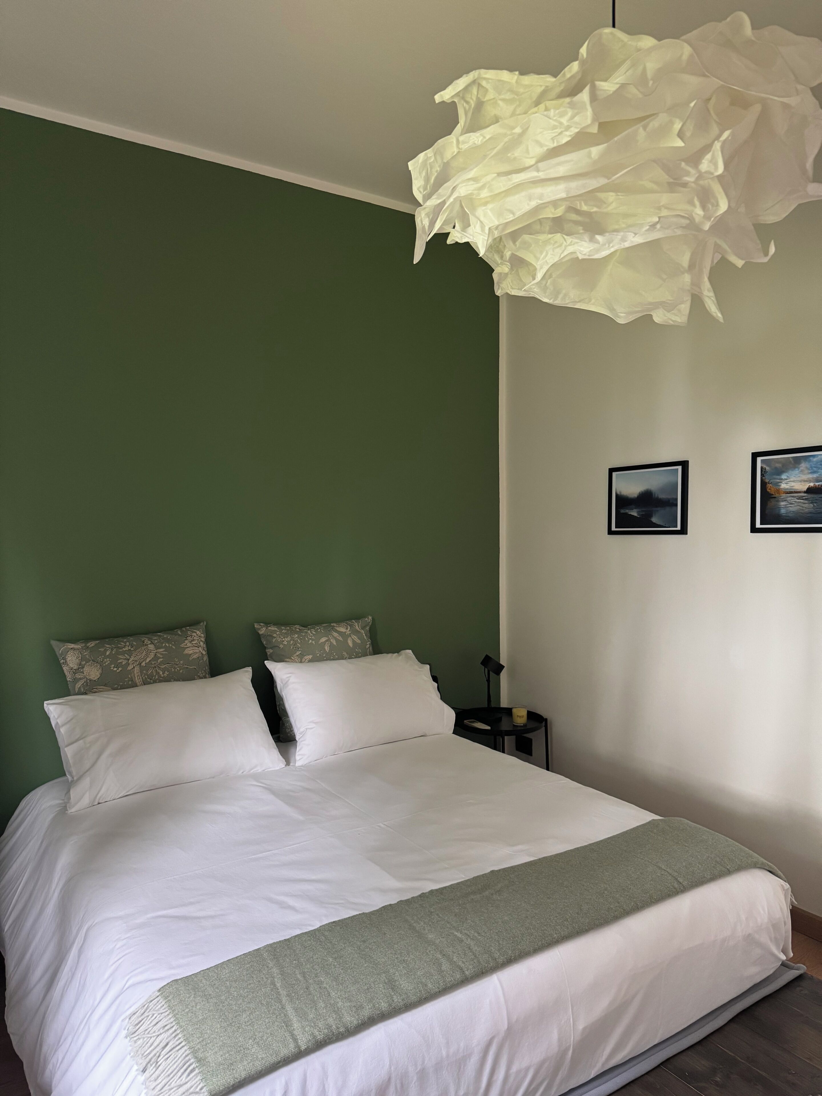 Ein ordentlich bezogenes Bett mit weißen Leinen, eine grüne Wand und zwei gerahmte Bilder an der Wand.