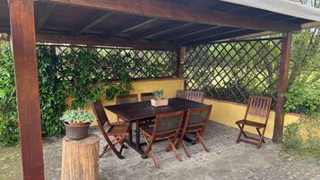 Une pergola en bois, avec une table et des chaises, entourée de verdure.