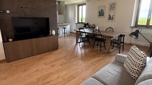 A modern living room with a TV, sofa, and dining area. - Accogliente appartamento immerso nel parco del Ticino (Castelnovate)