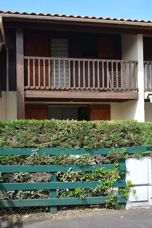 Ein zweistöckiges Gebäude mit Balkon, grüner Umzäunung und weißem Technikschacht.