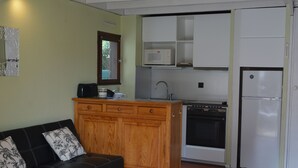 A compact kitchen with a built-in oven, microwave, and refrigerator. A wooden cabinet with drawers is adjacent to the kitchen, and a black leather sofa with floral cushions is in the foreground. - L'ANCRE BLEU ENTRE FILET ET MAREE; HOUSE IN THE HEART OF CAPBRETON HARBOR (Capbreton)