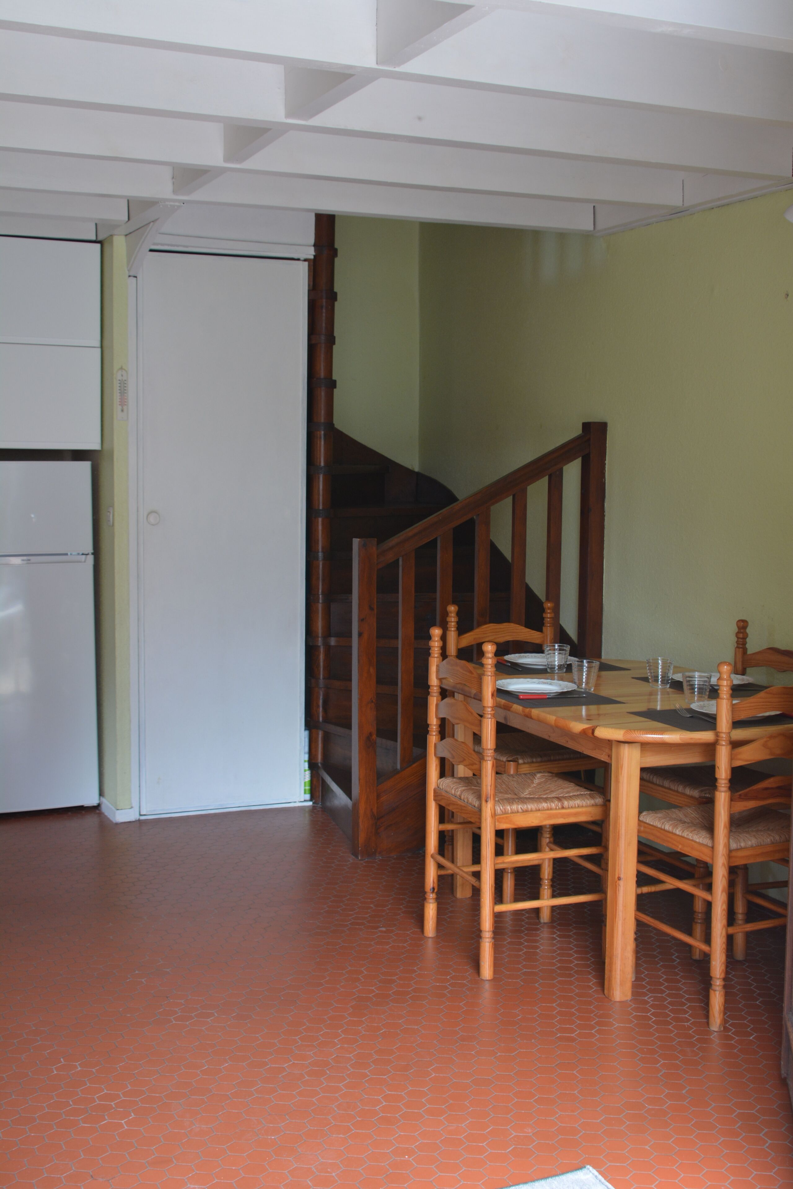 Ein Essbereich mit Holztisch und -stühlen, einem weißen Kühlschrank und einer Treppe, die zu einer oberen Ebene führt.