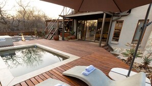 Ein Poolbereich mit Holzterrasse, Liegestühlen und einer überdachten Sitzgelegenheit.