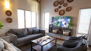 Ein Wohnzimmer mit grauem Sofa, einem Couchtisch, einem Fernseher und dekorativen Tellern an der Wand.