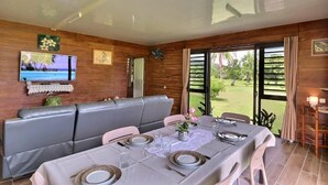 Zona pranzo con tavolo imbandito per quattro persone, divano, televisione e vista su un giardino.
