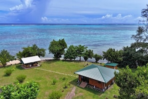 Une propriété située sur la côte, comprenant une cabane en bois et une construction plus petite, le tout entouré d’une végétation luxuriante et offrant une vue sur l’océan.