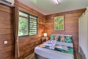 A wooden-paneled room with a bed, a window, a lamp, and a painting.