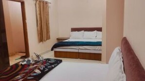 A bedroom with a bed, a nightstand, a window with curtains, and an air conditioning unit. - Kanha Homestay Near Mahakal Mandir (Ujjain)
