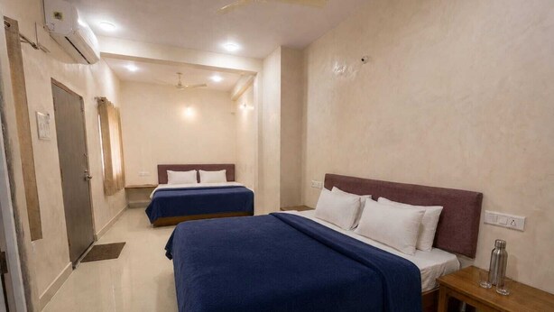 A hotel room with two beds, a wooden nightstand, a ceiling fan, and an air conditioning unit. - Kanha Homestay Near Mahakal Mandir (Ujjain)