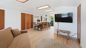 Ein modernes Wohnzimmer mit einer Couch, einem an der Wand montierten Fernseher und einem Essbereich mit Stühlen und einem Tisch.