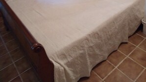Una camera da letto con un letto in legno, una coperta bianca e un solo cuscino.