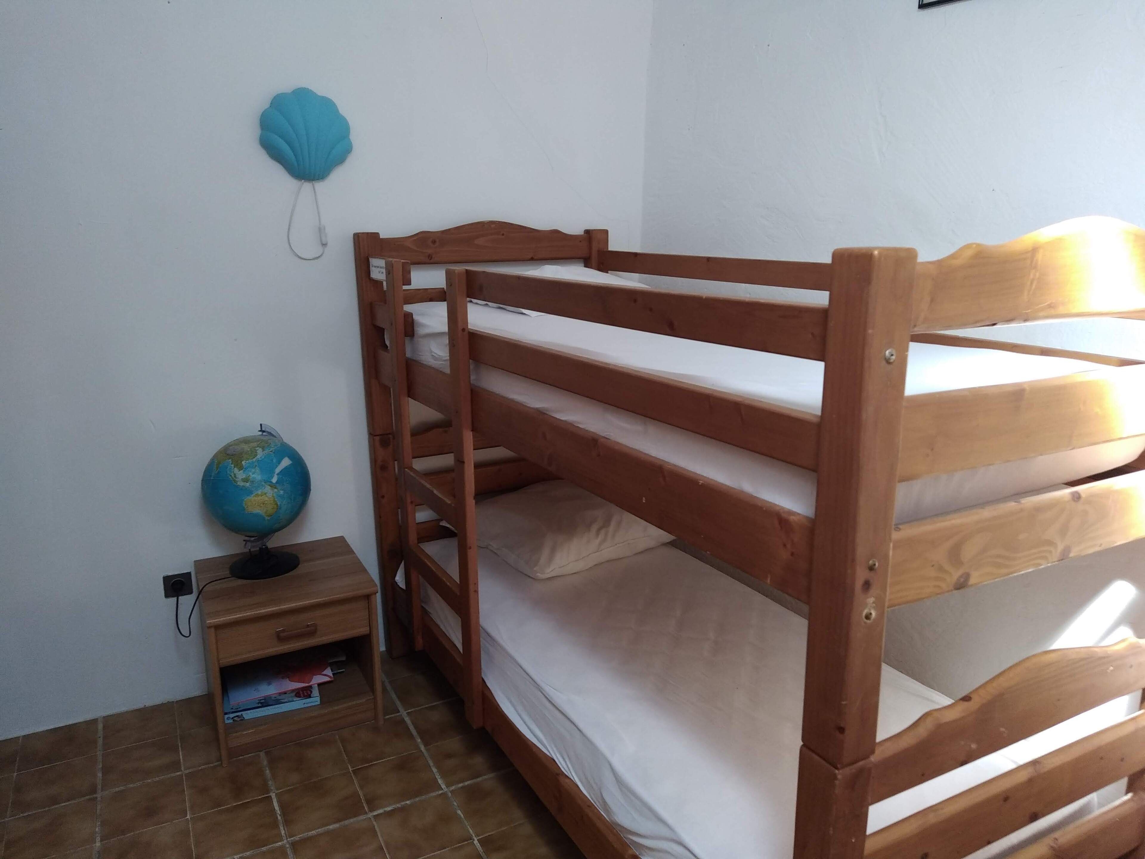 Una cama litera con estructura de madera, una mesita de noche con un globo terráqueo y un estante fijado a la pared.