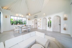 Un interior amplio con comedor, mobiliario blanco y ventanas grandes.