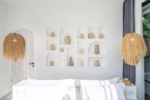 Un dormitorio moderno con una cama, un estante montado en la pared con objetos decorativos, y dos lámparas colgantes.