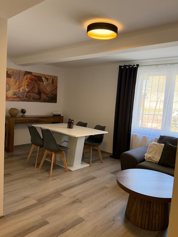 Una sala de estar moderna con comedor, un cuadro en la pared y un ventanal con cortinas.
