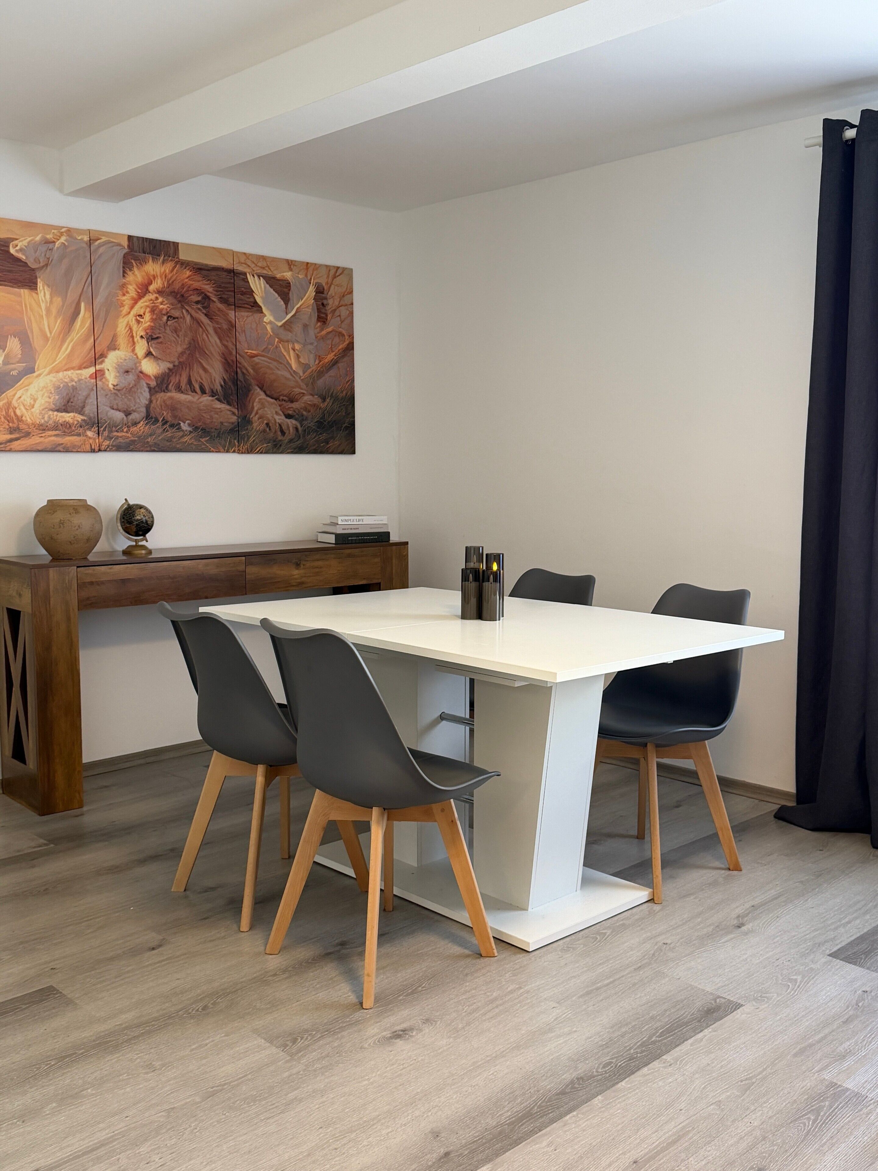 Un espace repas moderne avec une table blanche, des chaises noires, un buffet en bois et un grand tableau accroché au mur.