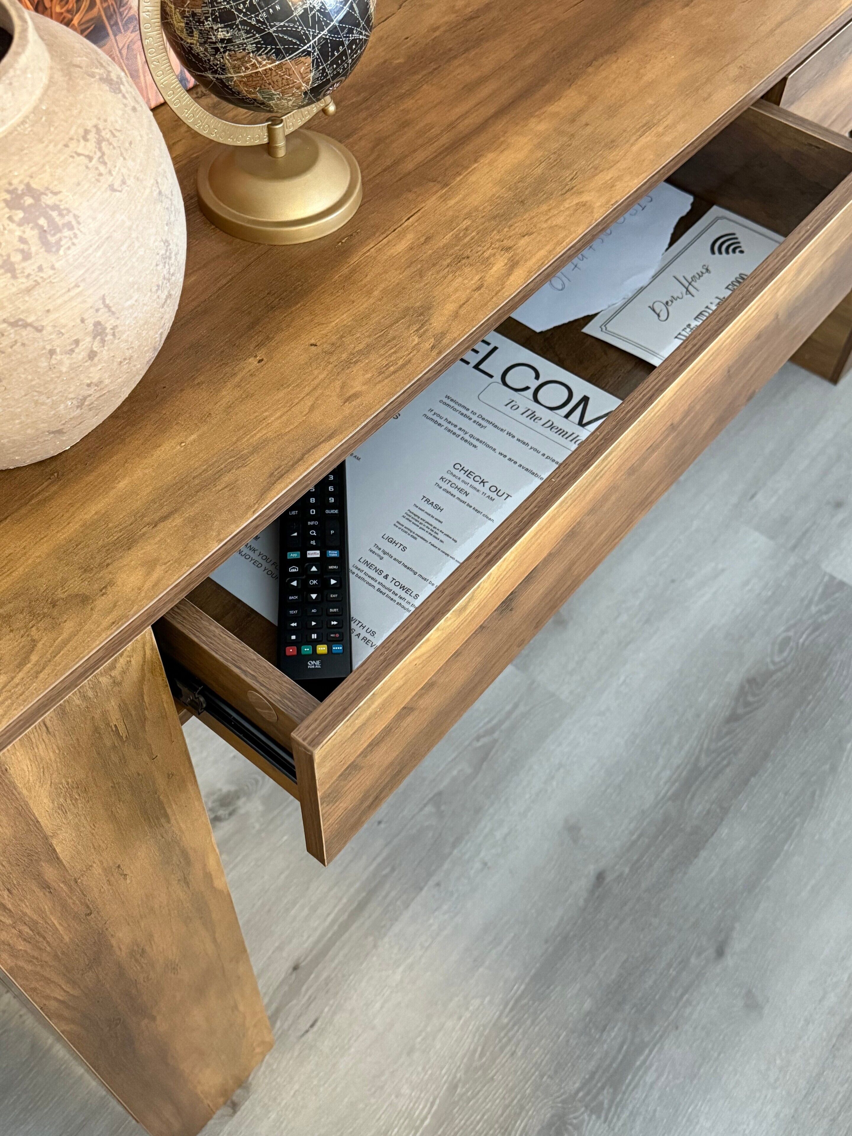 Ein Holztisch mit Globus, einer Vase und einer Schublade, in der sich eine Fernbedienung und eine Willkommenskarte befinden.