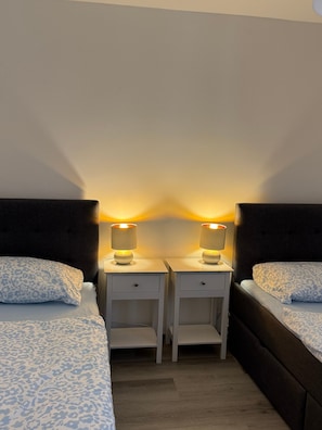 Ein Hotelzimmer mit zwei Betten, jeweils mit Kopfteil, und zwei Nachttischen mit Lampen.