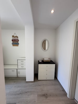 Una habitación con un escritorio blanco, un aparador negro, un espejo y un cartel en la pared con frases motivacionales.