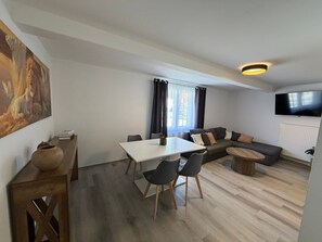 Una sala de estar moderna con una mesa de comedor, sillas, un sofá y un televisor.