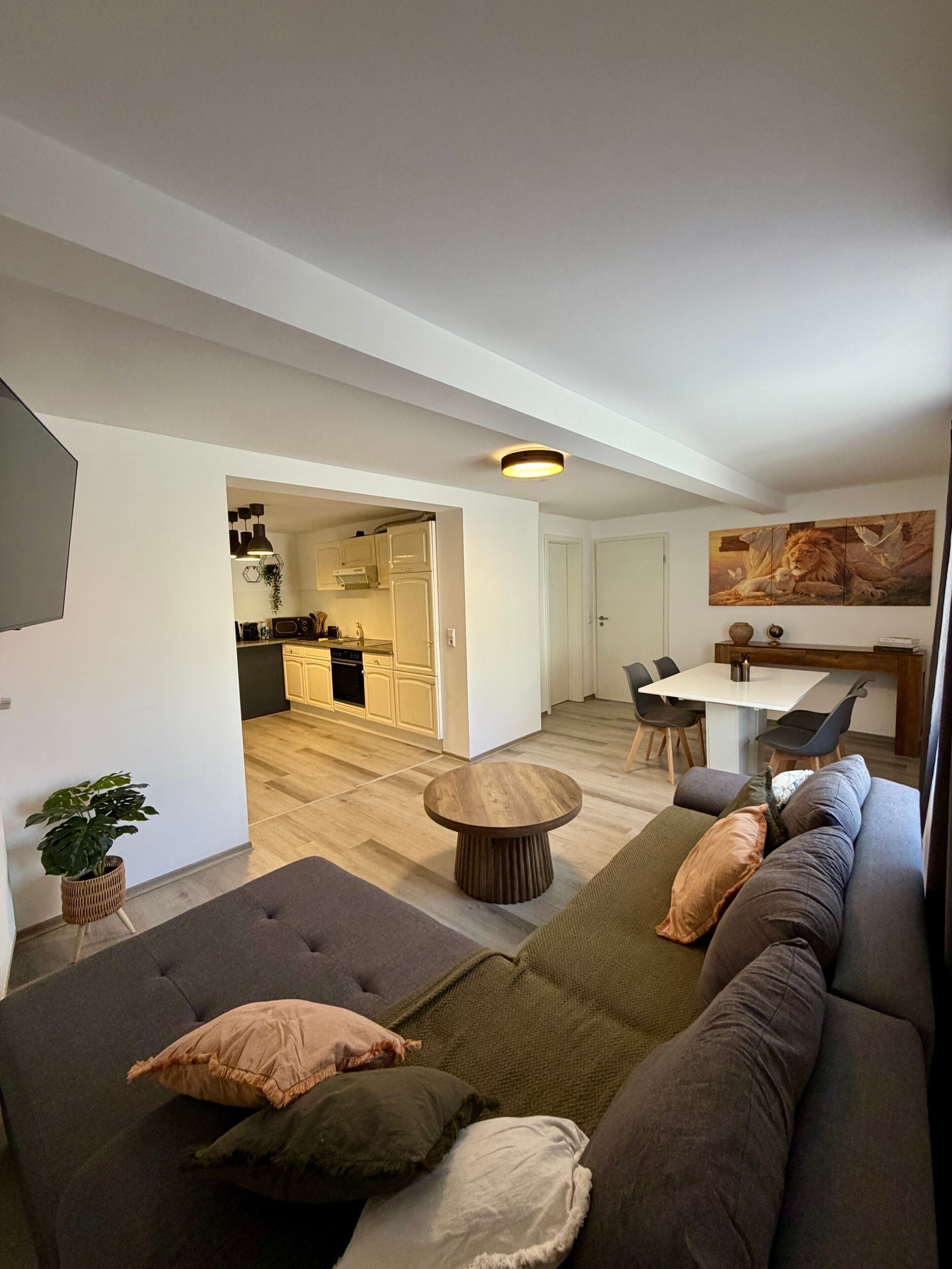 Ein modernes Wohnzimmer mit einer Couch, einem Essbereich und einer Küche im Hintergrund.