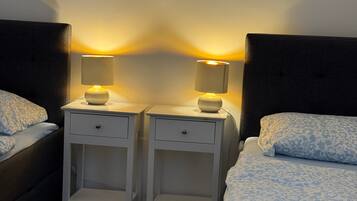 Un dormitorio con dos mesitas de noche, cada una con una lámpara, una cama con edredón estampado y suelo de madera.
