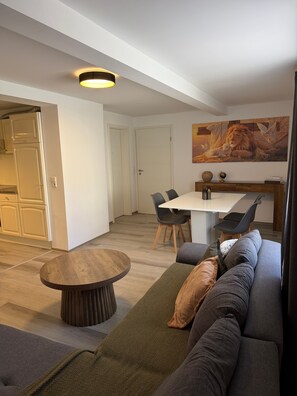 Una sala de estar moderna con un sofá, una mesa redonda de madera y un comedor con sillas.