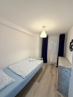 Una habitación pequeña con una cama individual, suelo de madera, techo blanco y una lámpara colgante.