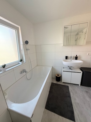 Ein modernes Badezimmer mit einer Badewanne, einem Fenster, einem Waschbecken und einem Spiegel.