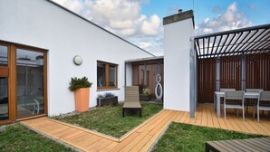 A modern outdoor patio area with a wooden deck, a seating area, and a pergola with seating. - RentPlanet - Apartament Wschodnia (Kołobrzeg)