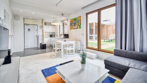 A modern living room with a grey sofa, a white coffee table, and a dining area with a white table and chairs. - RentPlanet - Apartament Wschodnia (Kołobrzeg)