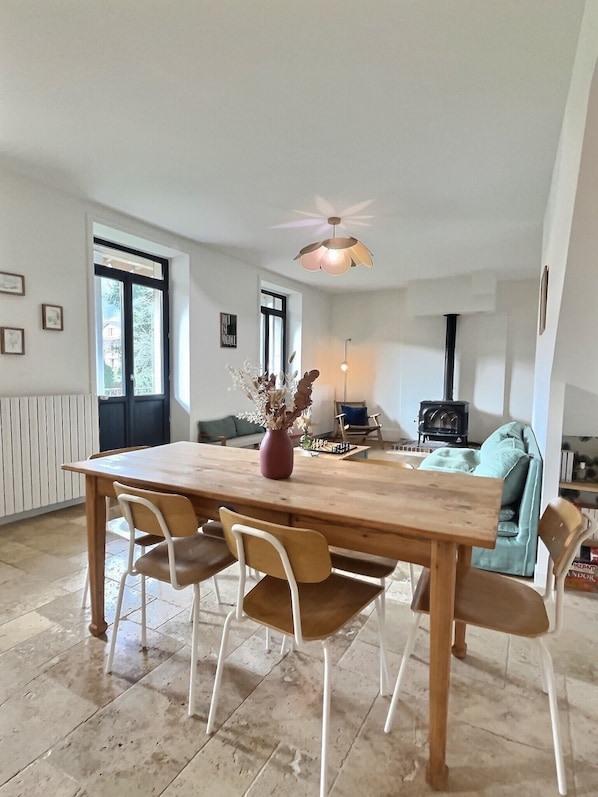 Un coin repas avec une table en bois, quatre chaises, un vase avec des fleurs et un ventilateur de plafond.