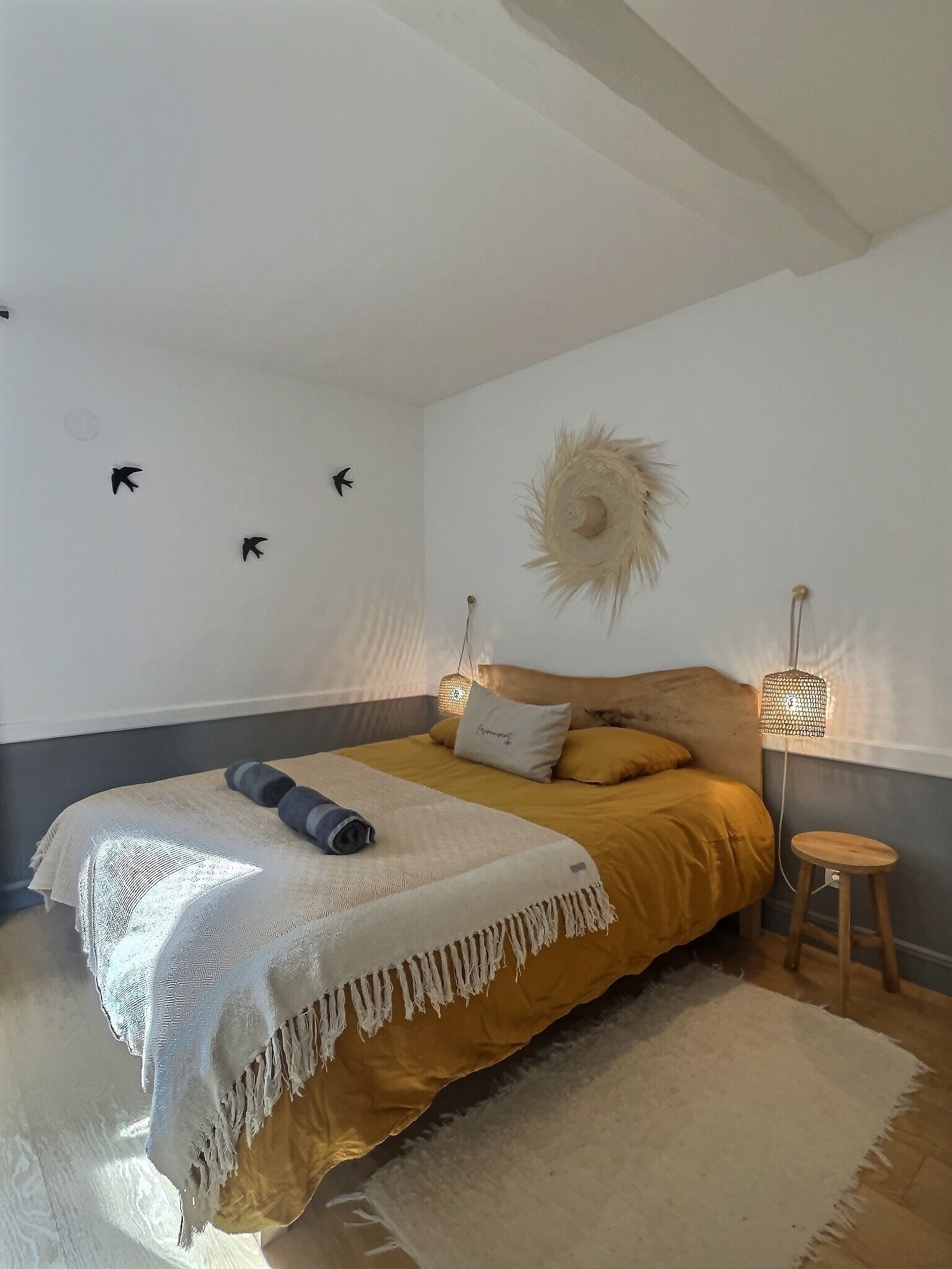 Una camera da letto con un letto, una lampada da comodino, una decorazione a parete e uno sgabello.