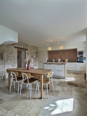 A modern kitchen with a central island, white cabinetry, and a stone accent wall. - "Le clos du bon temps" (Lugny)