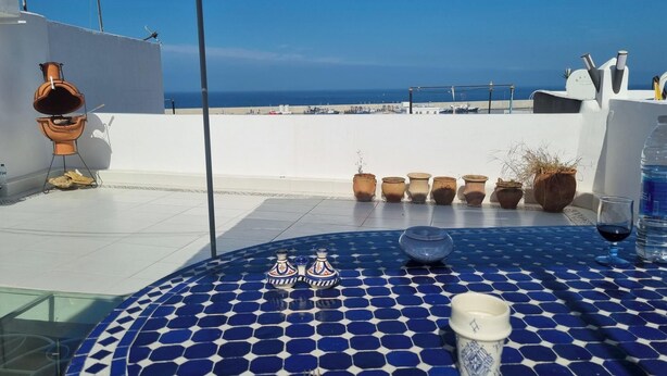 A terrace with a blue tiled table, potted plants, and a view of the sea. - Tangier medina Riad Sea view and Spain (Tanger)
