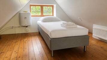 Une chambre avec un plafond en pente, une fenêtre donnant sur la verdure, un lit avec une literie blanche et un radiateur.