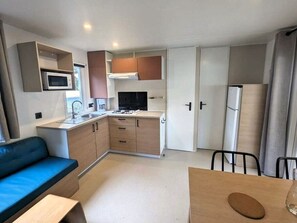A compact kitchenette with a microwave, stove, and refrigerator. There is a sofa and a dining table with chairs. - Cozy mobile home - 6 guests (Saint-Hilaire-de-Riez)